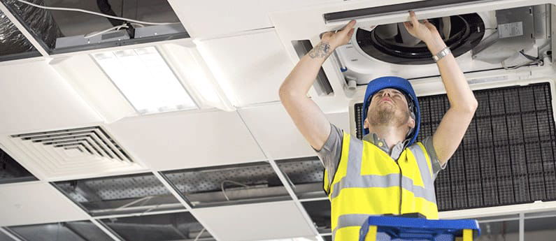 A man on a ladder works on an indoor overhead air system. 