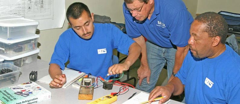 An instructor helps two HVAC students with an assignment 