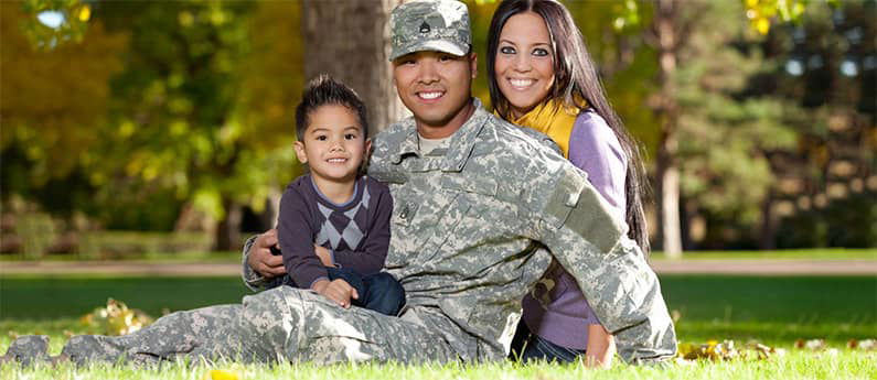 A smiling Military Family of 3, sitting on the grass in a park